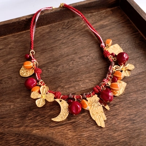 Dettaglio collana etnica con ciondolo a cuore e fiore e charms luna su corda rossa
