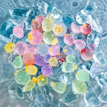 Close-up of translucent colorful resin fruit and flower charms in clear water with ice