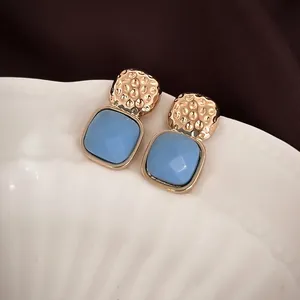 Elegant gold-plated square stud earrings with sky blue resin stones on a white tray