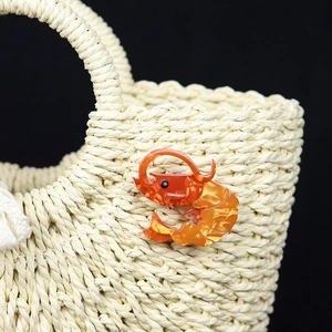 Chic orange acrylic lobster brooch pinned on a straw bag with a minimalist black background