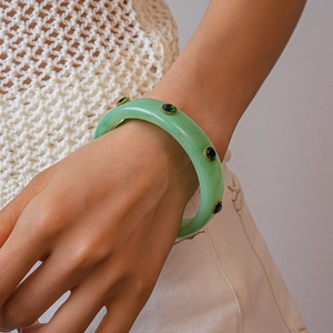 Close-up of light green acrylic bangle with emerald rhinestones in gold settings