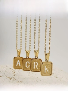 Détail de pendentifs carrés en acier plaqué or 18 carats avec texture de lettres mates
