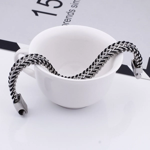 Detail eines Armbands aus Leder und Edelstahl, drapiert an einer weißen Tasse