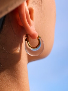 Close-up of a clear resin hoop earring with gold metal clasp against a blue sky