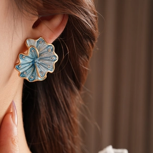 Close-up of vintage blue enamel flower earring with gold edges and crystals on model ear