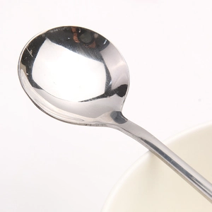 Cucchiaio a manico lungo in acciaio lucido su ciotola bianca per caffè o dessert fini