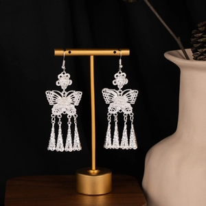Macro detail of silver butterfly tassel earrings with floral motifs on a display stand