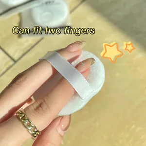 Soft cotton powder puff with two-finger ribbon handle shown in hand for makeup setting