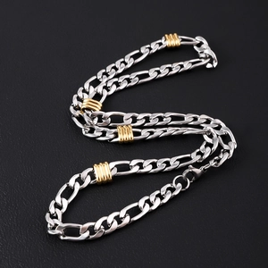 Macro view of silver stainless steel Figaro necklace with gold bead accents on black background