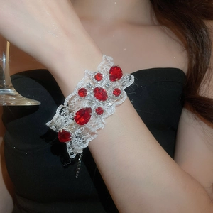 Détail d'un bracelet en dentelle blanche orné de cristaux rouges et d'accents argentés