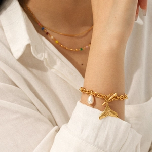 Detailaufnahme eines goldenen Gliederkettenarmbands mit Fischschwanzanhänger und Perle