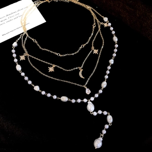 Detail of layered gold necklace with star, crescent moon pendants and baroque pearls