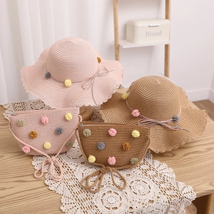 Detail of straw hat and matching bag set with colorful pom-poms and bow on a lace tablecloth