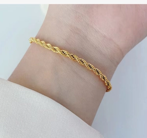 Detailed view of a gold-plated twisted rope chain bracelet on a person's wrist