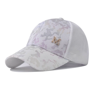 Detail of white mesh baseball cap featuring a golden M logo and camo pattern visor