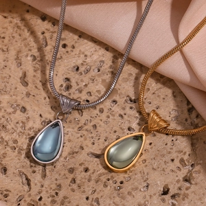 Detail of drop pendants in gold and silver finish with snake chains on stone texture