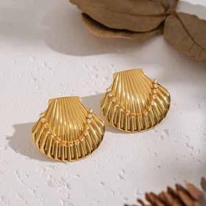 Gold shell stud earrings with rhinestones on a white textured background with autumn decor