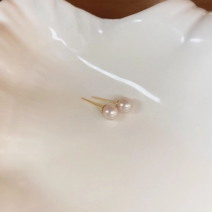 Close-up of elegant champagne pearl earrings on a white shell plate with golden posts