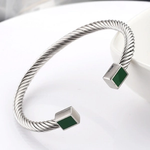 Detail of twisted silver metal cuff with green gemstone inlays on a white surface