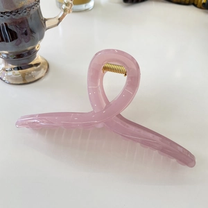 Macro shot of 15cm pink acrylic shark hair clip with a golden metal spring on white surface