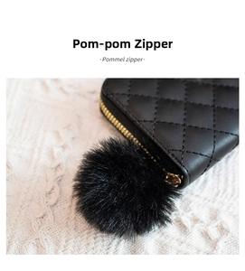 Dettaglio borsa in pelle nera trapuntata con zip dorata e ciondolo pompon di pelliccia