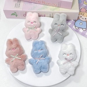 Vue à plat de cinq breloques lapins en peluche colorés avec nœuds sur un plateau blanc