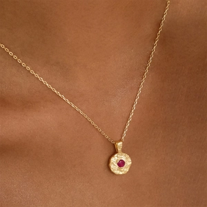 Irregular gold birthstone pendant necklace with red gem shown on a model neck