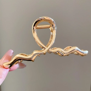 Close-up of golden wavy metal hair claw clip with polished finish and strong spring