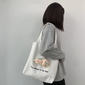 Close-up of white canvas tote bag featuring 3D cartoon plush doll and artistic print