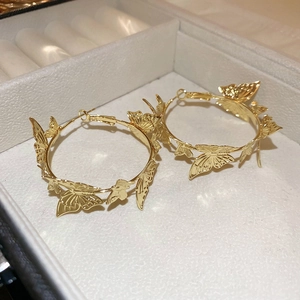 Close-up of golden hoop earrings featuring delicate 3D butterfly charms in a jewelry box