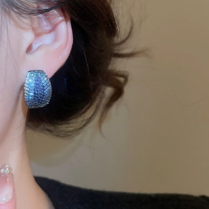 Close-up of blue and white gradient zircon C-shaped earrings worn on an ear