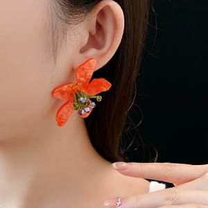 Close-up of orange floral earrings with purple beads on model against black background