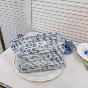 Detail of blue and white tweed makeup bag with woven texture and a simple wish label