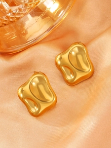 Detail of irregular gold earrings with lava texture on warm orange satin background