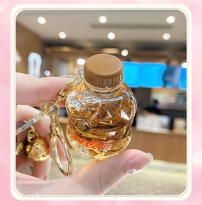 Detail of creative soda bottle keychain with golden bell and liquid-filled resin design