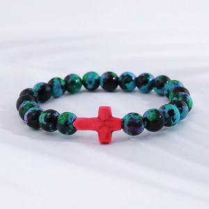 Detail of turquoise style beads with a red cross pendant on white textured fabric