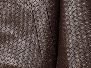 Detailed close-up of dark brown woven leather texture on a cropped jacket collar