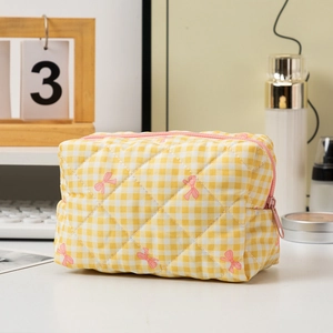 Borsa per cosmetici trapuntata a quadretti gialli con fiocchi rosa su una scrivania