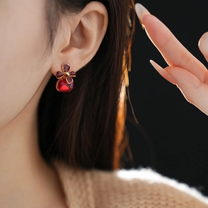 Detail view of gold flower earrings with a square red gemstone on a model ear
