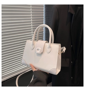 Detail of white crocodile embossed texture on a square handbag with elegant metal hardware