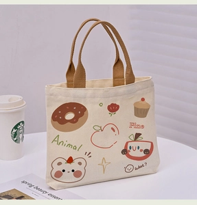 Close-up of canvas tote bag with cartoon illustrations and brown woven handles on a desk
