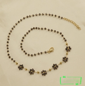Detail of dark grey beaded chain necklace with golden lobster clasp and flower charms