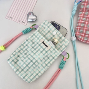 Detail of green plaid crossbody phone bag with pink braided rope strap and woven label