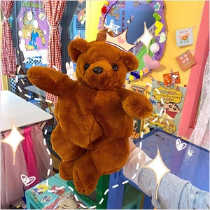 Detail shot of a brown plush teddy bear backpack held by hand in a cozy bedroom setting