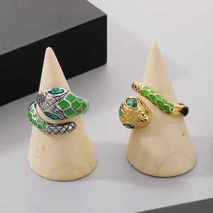 Detail of snake rings featuring green enamel scales and gemstone eyes on wood stands