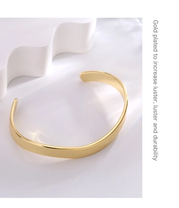 Detail of a minimalist gold-plated open bangle featuring a polished surface and sleek design