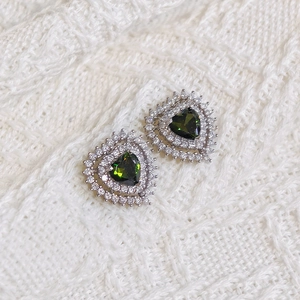 Detailed macro view of heart-shaped earrings with green gemstone and white zircon stones