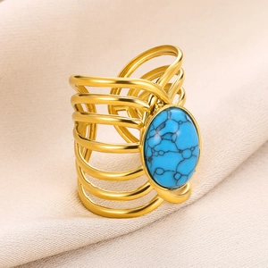 Détail d'une bague large dorée avec une grande turquoise ovale sur un tissu beige