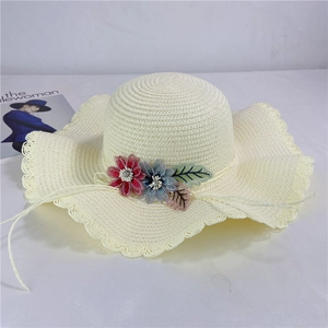 Close-up of beige straw sun hat with wavy brim and colorful floral decorations