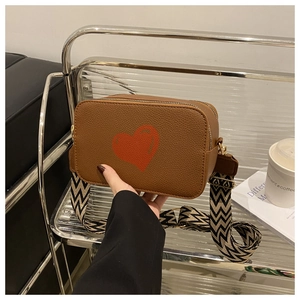 Detailed view of brown litchi pattern bag with red heart and woven wide shoulder strap